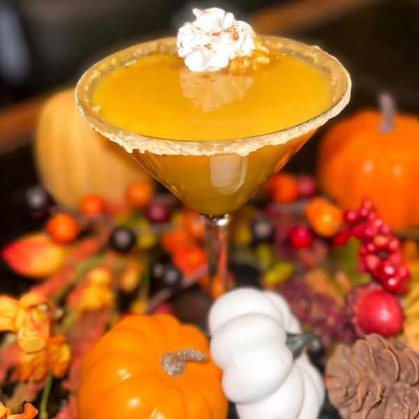 A pumpkin martini with whipped cream, surrounded by fall decorations like pumpkins and berries.