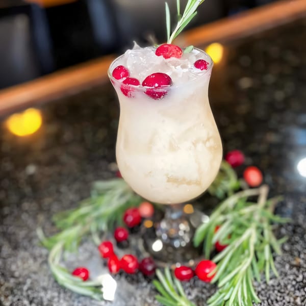 A House of Japan cocktail with ice, cranberries, and a rosemary sprig on a dark bar.