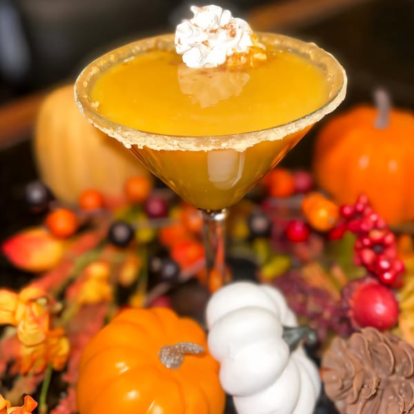 Pumpkin martini with whipped cream and cinnamon, surrounded by autumn decor like pumpkins and berries.