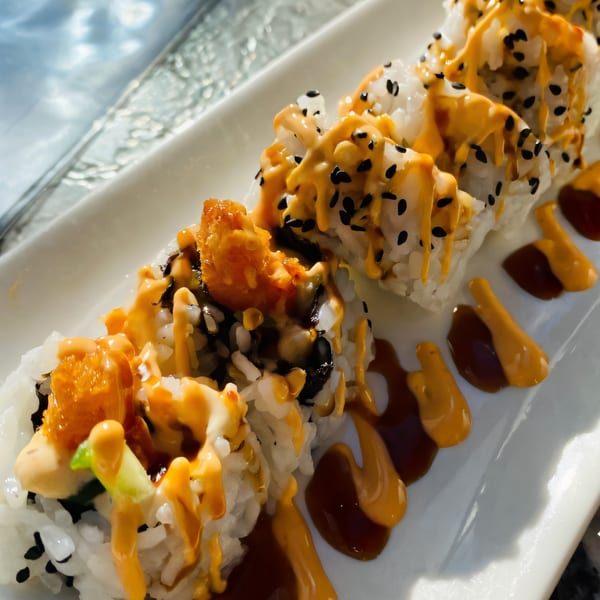 Close-up of House of Japan's sushi rolls topped with orange sauce and black sesame seeds.