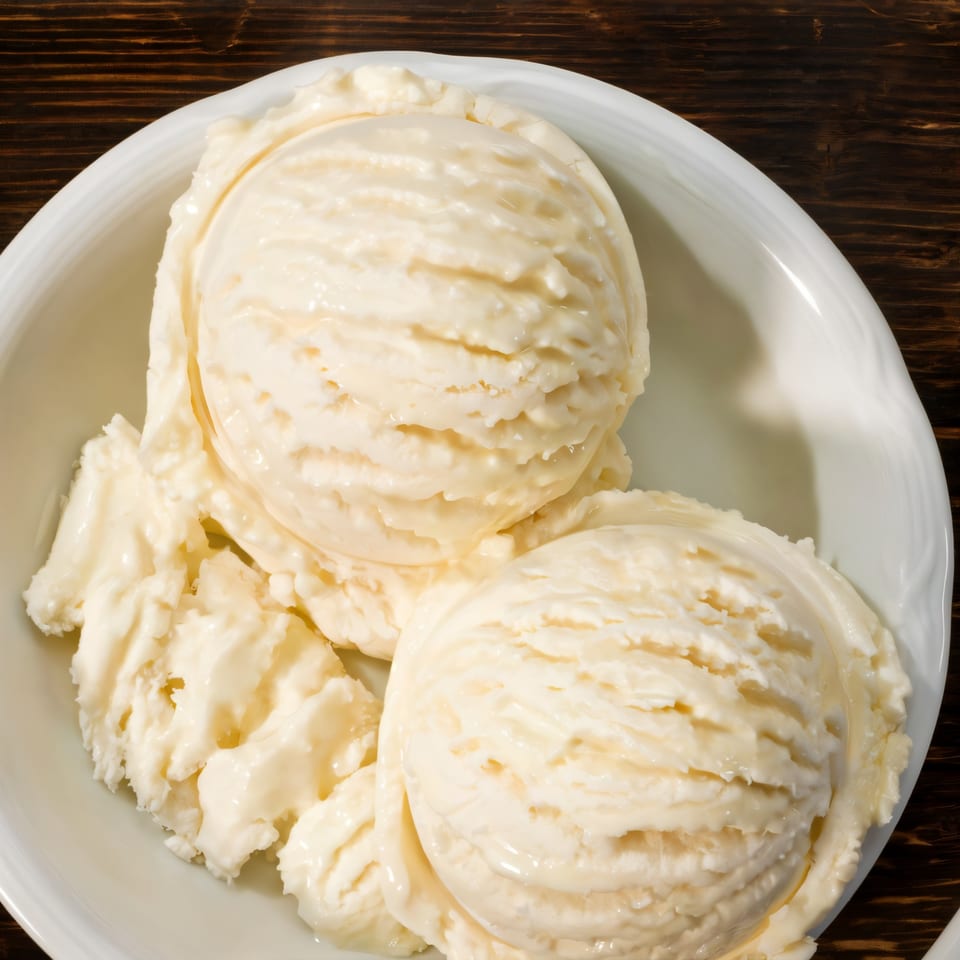 Three scoops of creamy vanilla ice cream in a white bowl on a dark wooden table.