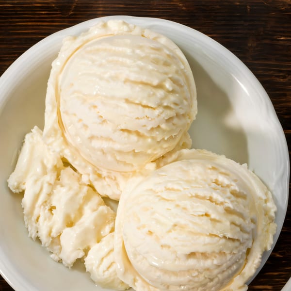 Three scoops of vanilla ice cream in a white bowl on a dark wooden table.