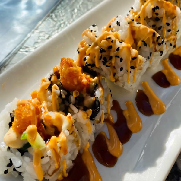House of Japan's sushi rolls with orange sauce and black sesame seeds on a white plate.