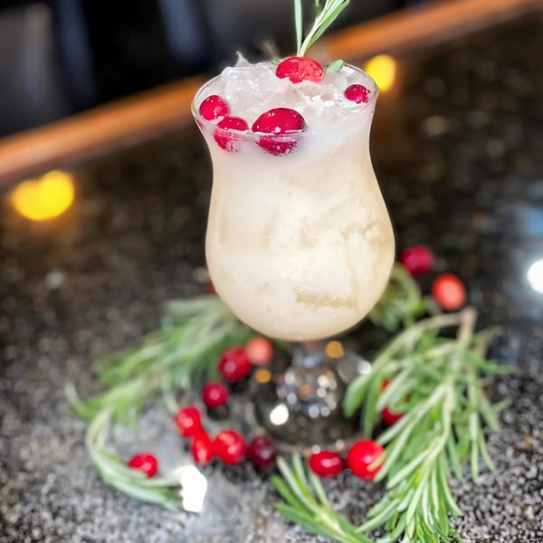 A festive cocktail with ice, cranberries, and rosemary garnish on a dark bar surface.