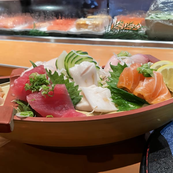 A wooden boat-shaped dish filled with various sashimi, including tuna, salmon, and white fish.